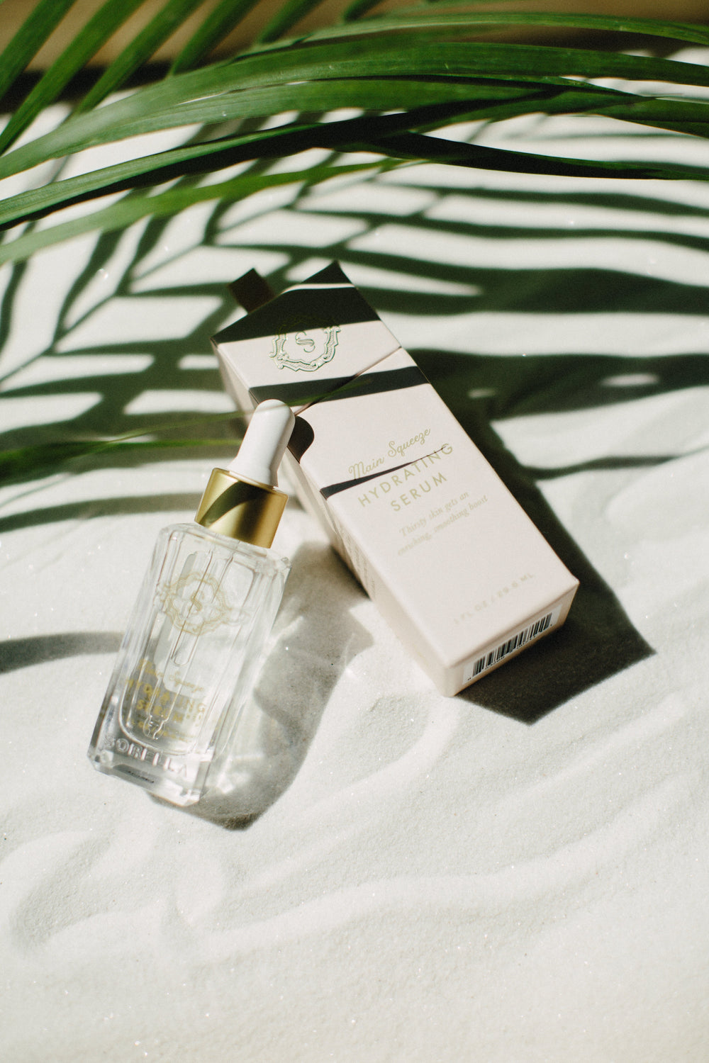 Main Squeeze Hydrating Serum in sand under a palm leaf