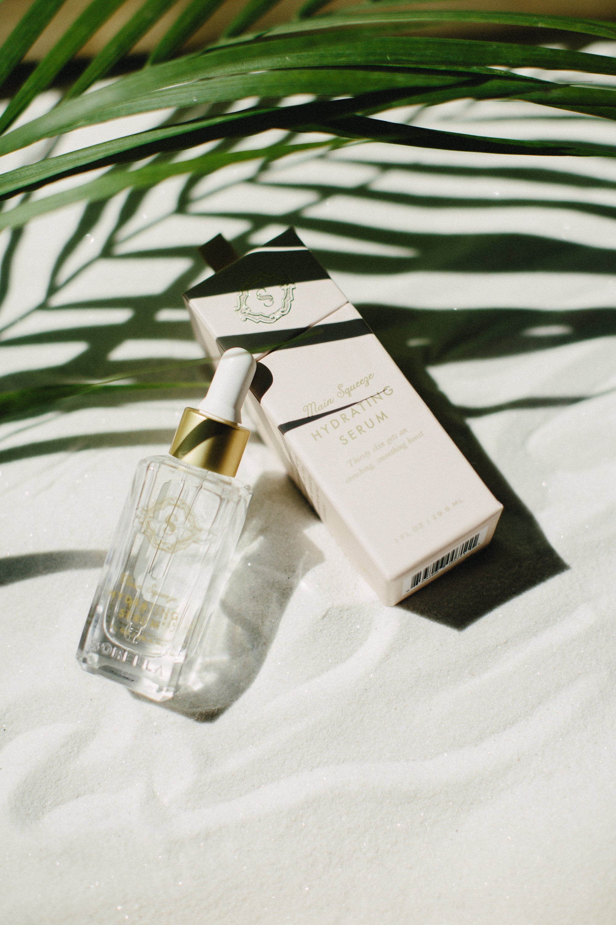 Main Squeeze Hydrating Serum in sand under a palm leaf