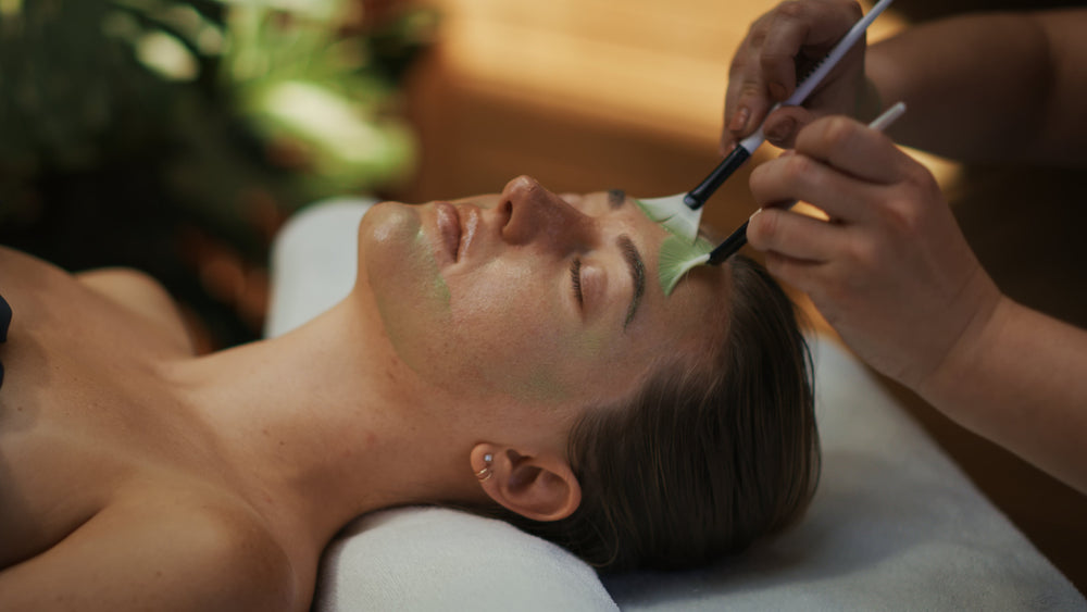 Person receiving a facial treatment with a brush applying product to their face.