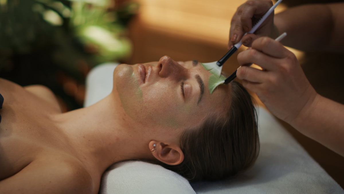 Person receiving a facial treatment with a brush applying product to their face.